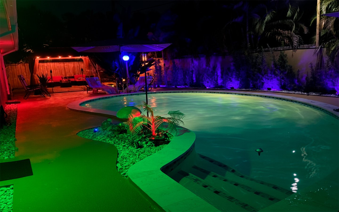 Nighttime view of Garden of Manors’ heated pool, featuring ambient LED lighting, tropical landscaping, and a serene island centerpiece designed for relaxed evening swims.